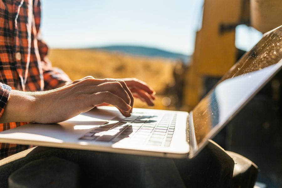 Landwirt arbeitet am Laptop vor Getreidefeld.
