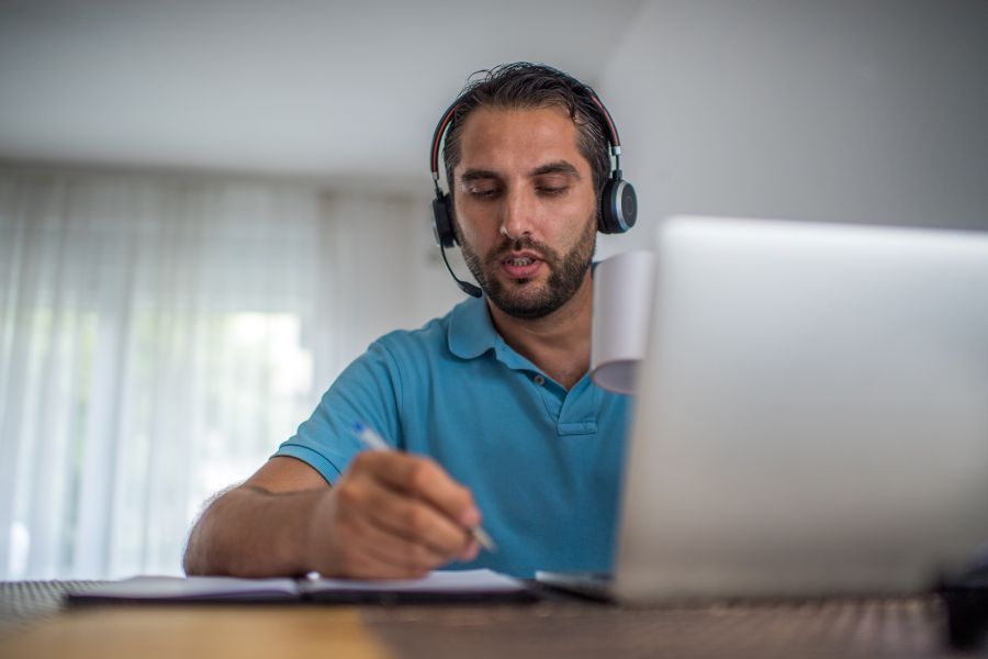 Ein Mann mit Kopfhörern auf dem Kopf sitzt vor einem Notebook.