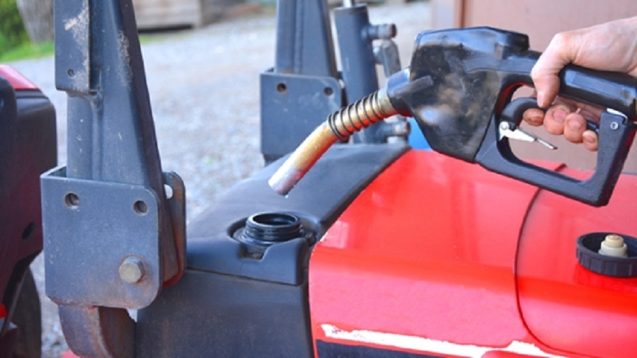 Ein Zapfhahn nähert sich der Tanköffnung eines roten Traktors, um ihn zu  betanken.