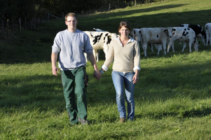 Junges Paar geht Hand in Hand über Weide mit schwarzbunten Rindern