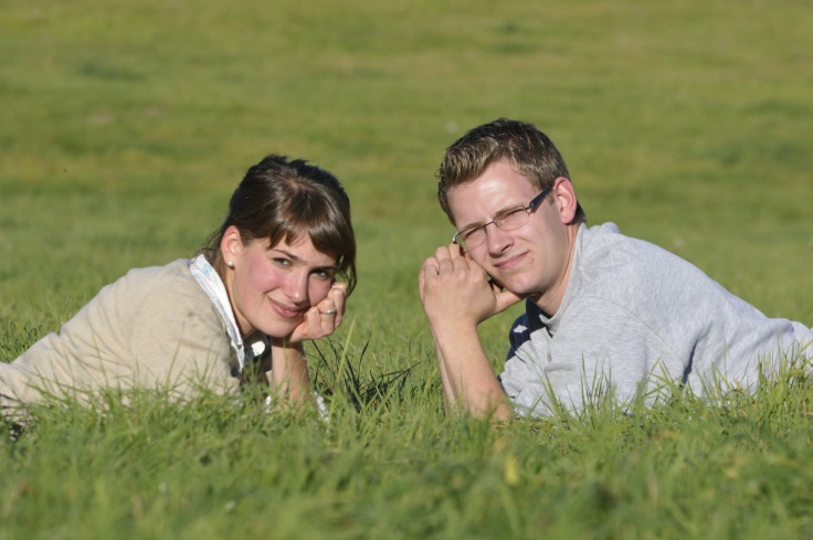 Junges Paar liegt sich gegenüber auf der Weide und schaut in die Sonne.