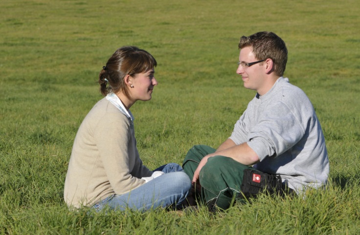 Junges Paar sitzt sich auf der Weide gegenüber und schaut sich gegenseitig an.