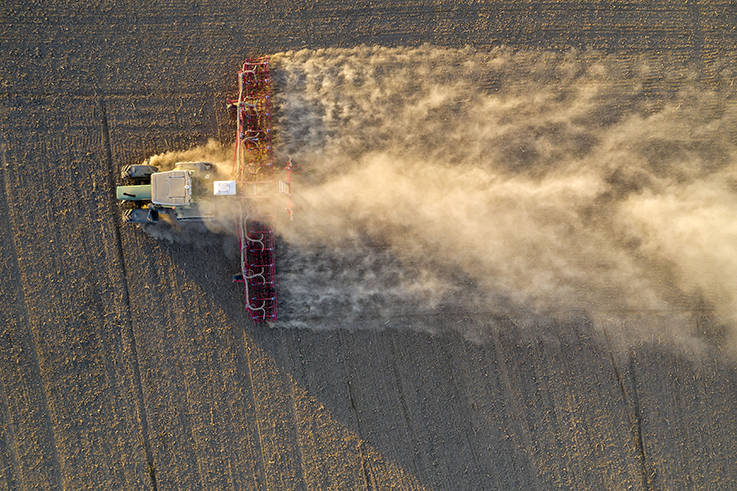 Luftbild von einem Traktor bei der Aussaat. Aufgrund der extremen Trockenheit kommt es zu starker Staubbildung.