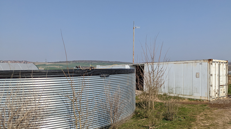 Zu sehen ist ein runder Wassertank mit einem Container links daneben.
