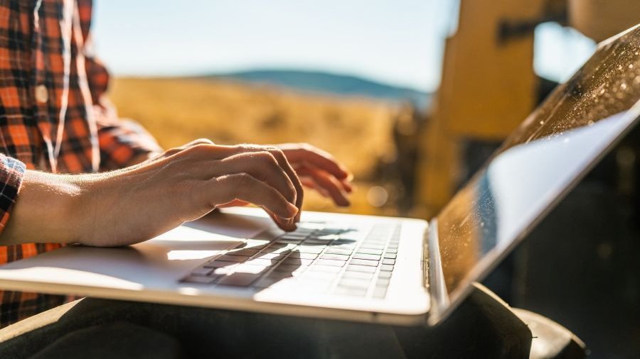 Landwirt arbeitet am Laptop vor Getreidefeld.