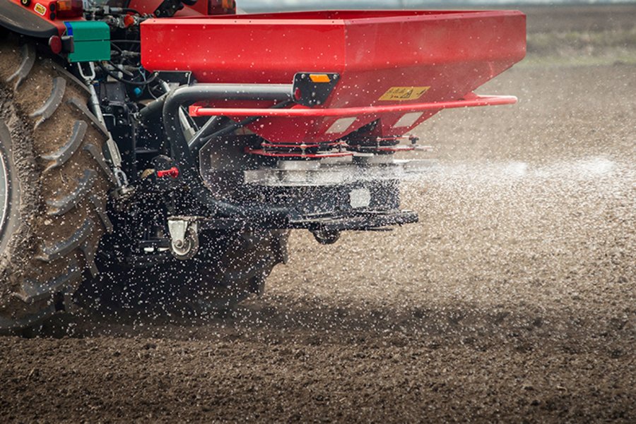 Traktor mit Düngerstreuer fährt über den Acker.