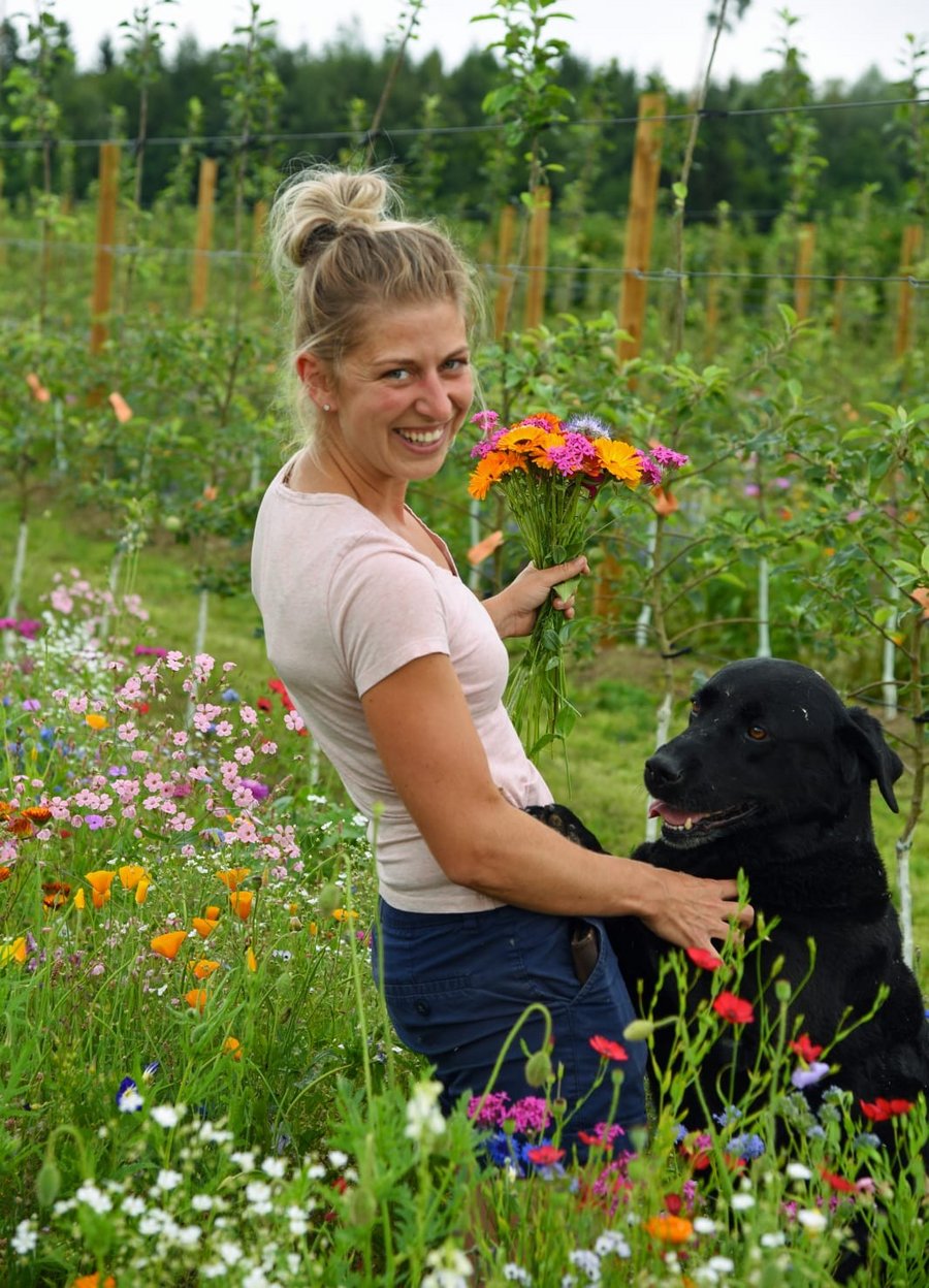 Zu sehen ist Lena Nüberlin in einer Blumenwiese mit Hund und Blumenstrauß in der Hand.