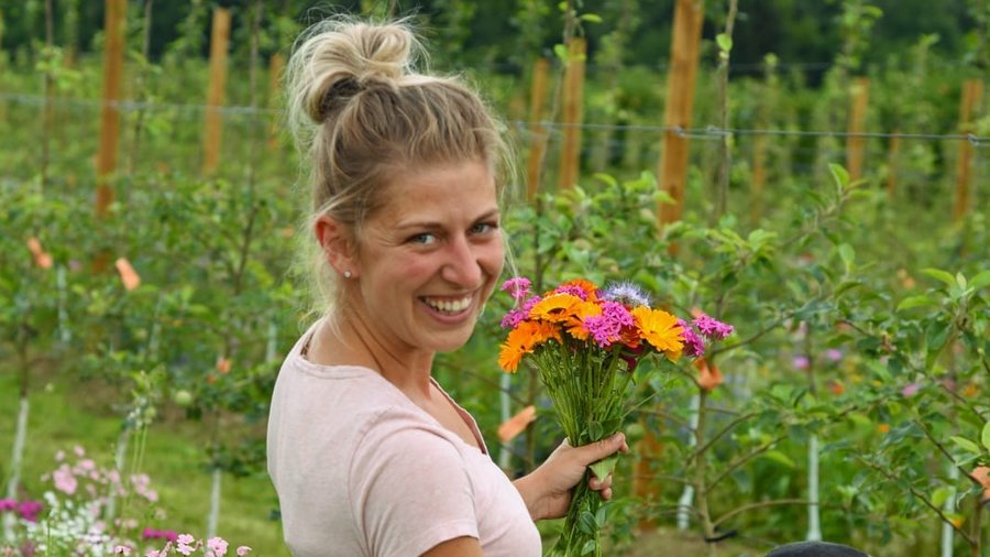 Zu sehen ist Lena Nüberlin in einer Blumenwiese mit Hund und Blumenstrauß in der Hand.