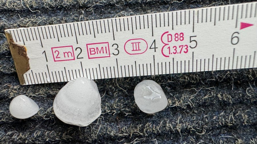 Die Größe von drei Hagelkörnern wird anhand eines Zollstocks gemessen.