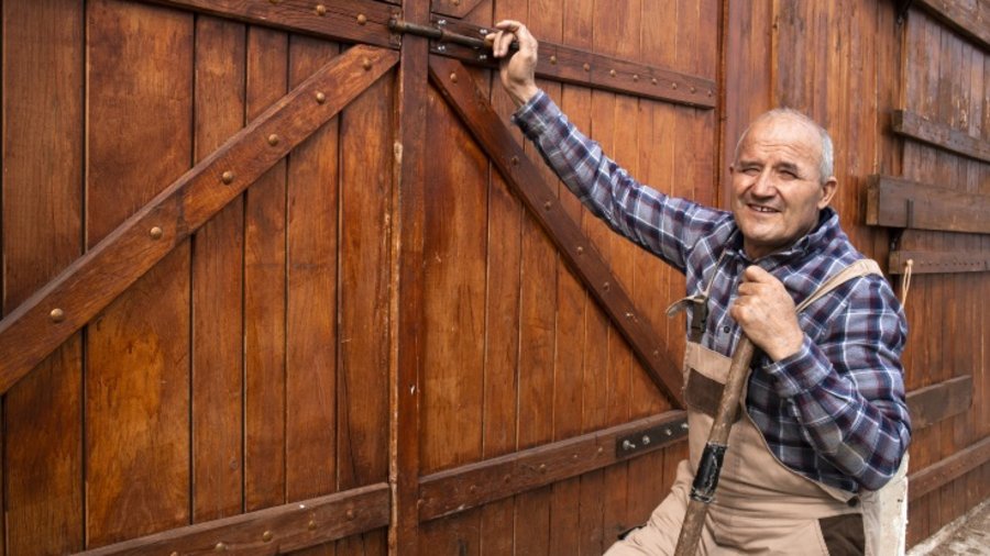 Älterer Bauer schließt Scheunentor und damit symbolisch seinen Bauernhof