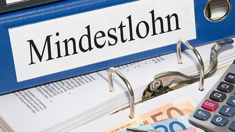 Ausschnitte von Ordnerrücken mit Aufschrift „Mindestlohn“, von darunterliegendem aufgeklappten Ordner, von Euro-Geldscheinen, silbernem Kugelschreiber und Taschenrechner.