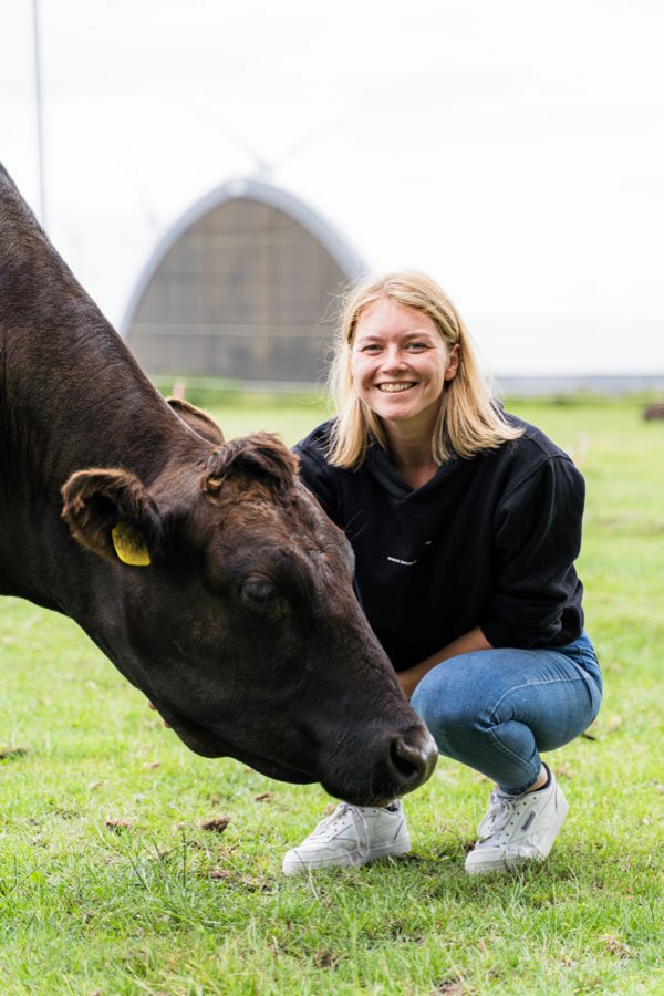 Lanwirtin hockt auf einer Wiese vor einem Rind.
