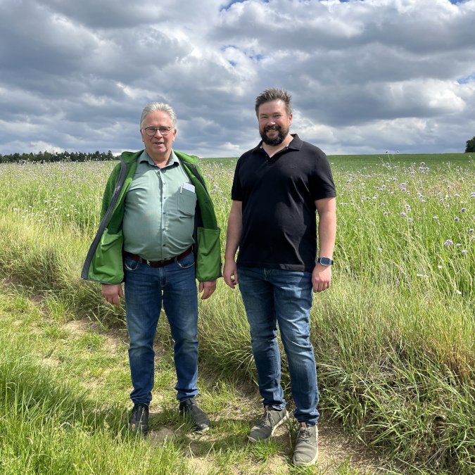 Ganzkörperfoto der beiden Betriebsleiter vor einem Feld.