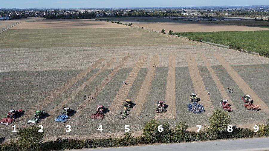 Mehrere Maschinen zur flachen Bodenbearbeitung stehen mit einer bearbeiteten Spur auf einem Feld.
