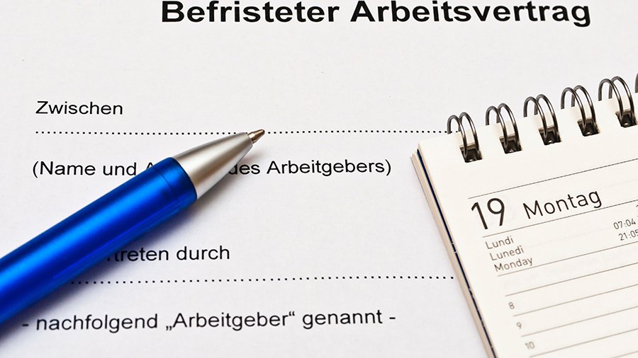 Ausschnitt von oberem Teil eines befristeten Arbeitsvertrages, obere Teile eines blauen Kugelschreibers und eines Tischkalenders mit Ringheftung sind sichtbar. 