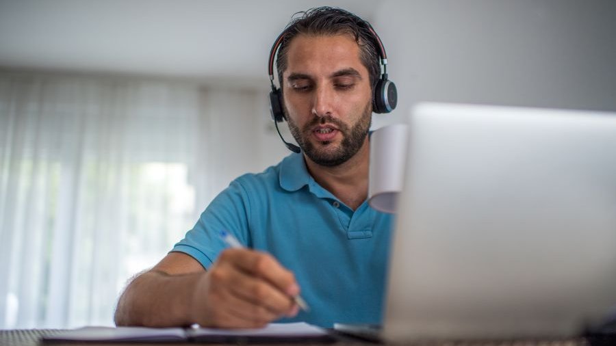 Ein Mann mit Kopfhörern auf dem Kopf sitzt vor einem Notebook.