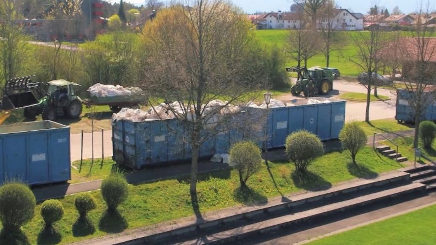 Sammelstelle mit blauen Containern, in denen Agrarfolien gesammelt werden. Dahinter Traktoren mit Hängern, die Folien anliefern. 