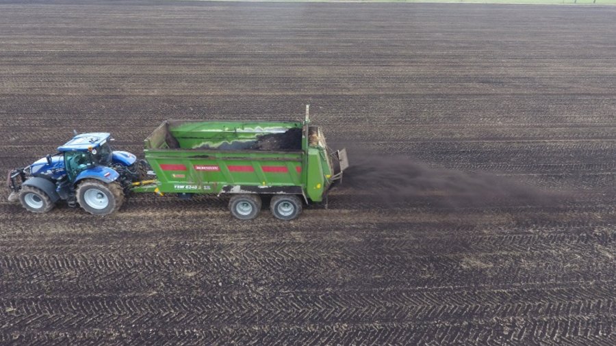 Traktor mit Anhänger bringt Kompost auf einem Feld aus. 