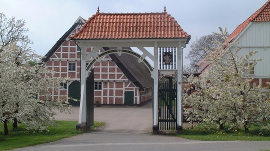 Fachwerkhaus mit davorstehendem weißen Torbogen und blühenden Bäumen