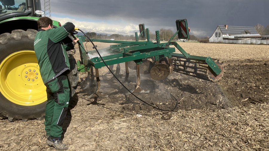 Eine landwirtschaftliche Maschine wird mit dem Hochdruckreiniger von Erdresten befreit.