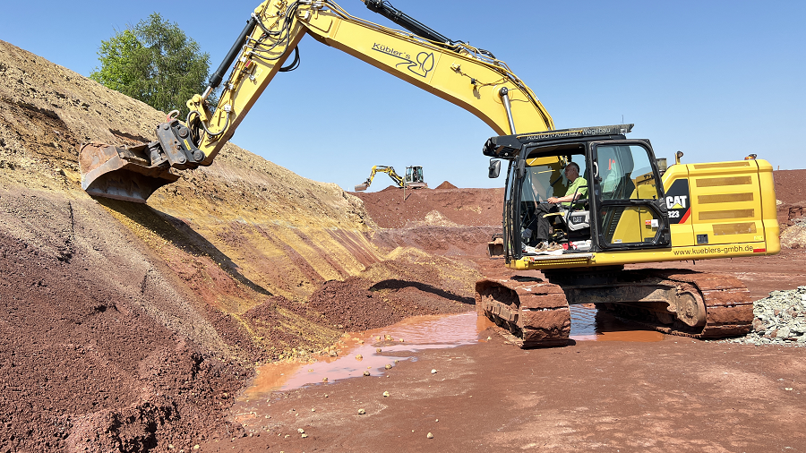 Zu sehen ist ein gelber Bagger bei den Erdarbeiten. Der Bagger steht am Fuß des Beckens und gräbt den Rand ab.