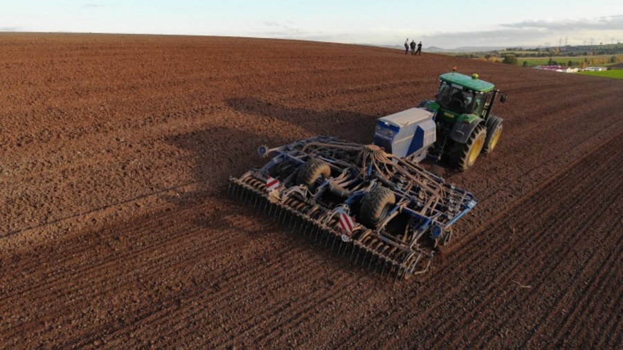 Ein Traktor mit einer aufgesattelten Drillmaschine bei der Herbstbestellung auf einer großen landwirtschaftlichen Nutzfläche. 