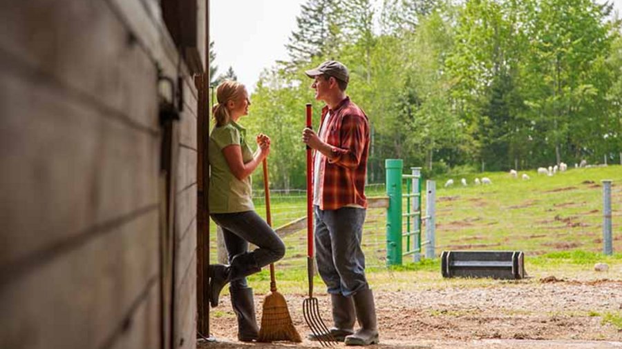 Eine Frau und ein Mann stehen mit Besen und Mistgabel im Freien.