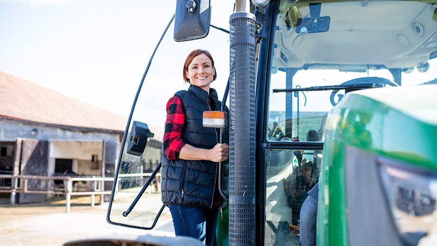 Frau steht auf Treppe eines grünen, neuen Traktors, schaut in Kamera.