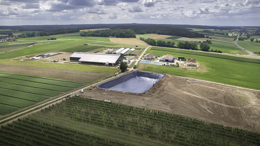 Zu sehen ist ein Erdfolienbecken in Vogelperspektive. Drumherum sind die Obstplantagen.