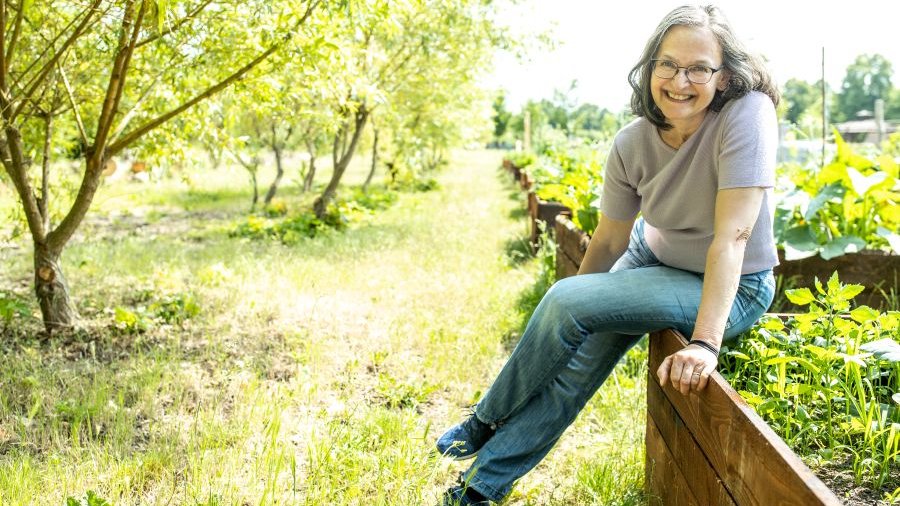 Frau sitzt auf einem Hochbeet in einem Garten. Klick öffnet Großansicht im neuen Fenster.