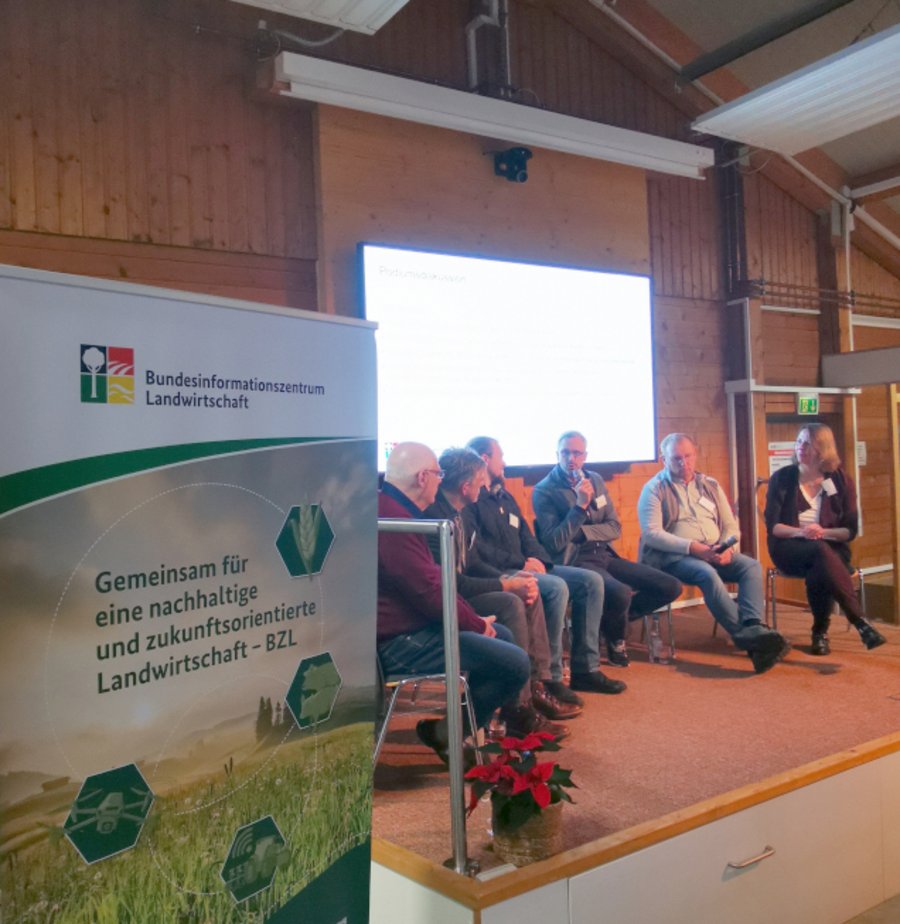 Sechs Personen sitzen auf einer Bühne im Halbkreis