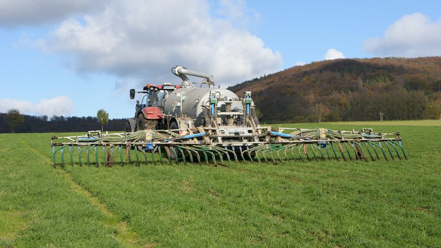 Schlepper mit Güllefass bringt Wirtschaftsdünger auf einem Feld aus, Gülleeinarbeitung mit angehängtem Grubber auf ein bearbeitetes Zwischenfruchtfeld im Frühjahr.