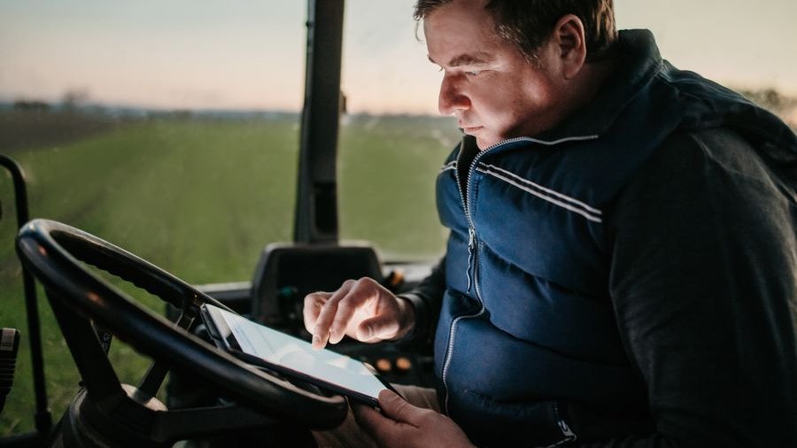 Landwirt sitzt auf Trecker und recherchiert etwas auf seinem Tablet.