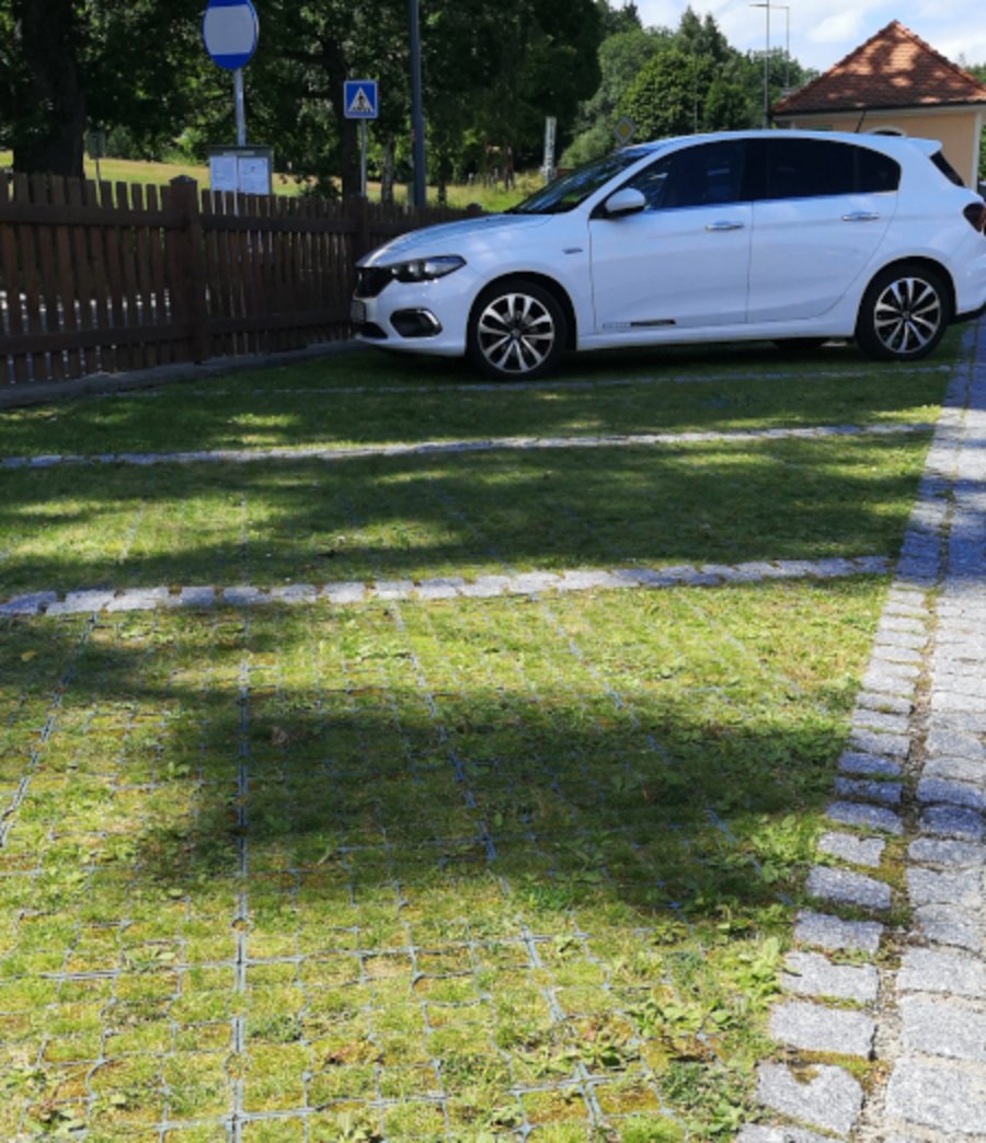 Ein Auto steht auf einer Parkfläche aus Rasengittersteinen. In den Steinen wächst Gras.