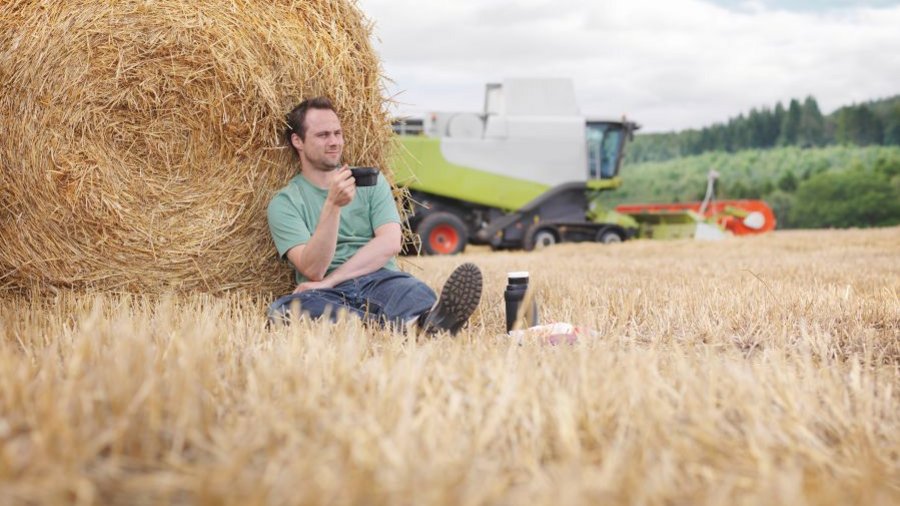 Mann sitzt vor Strohballen auf einem Stoppelfeld. Klick öffnet Großansicht im neuen Fenster.