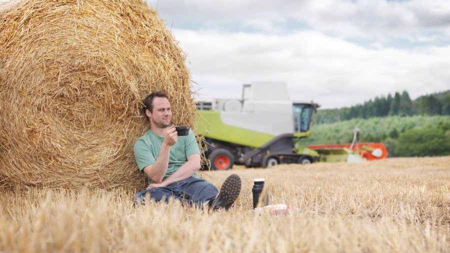 Mann sitzt vor Strohballen auf Stoppelfeld. Klick öffnet Großansicht im neuen Fenster.m