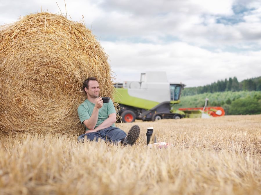 Mann sitzt vor Strohballen auf Stoppelfeld. Klick öffnet Großansicht im neuen Fenster.m