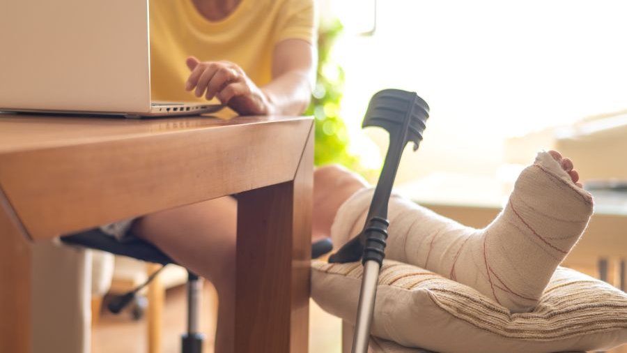 Frau mit eingegipsten Bein sitzt am Tisch.