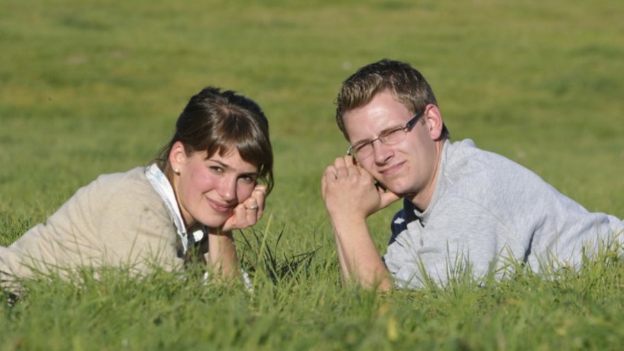 Junges Paar liegt sich gegenüber auf der Weide und schaut in die Sonne.