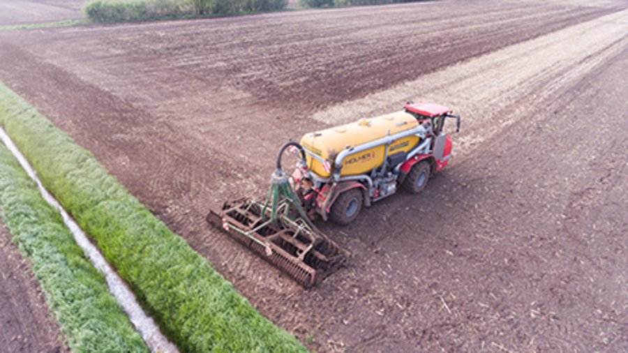 Traktor mit Miststreuer bei der Ausbringung von Gülle auf dem Acker